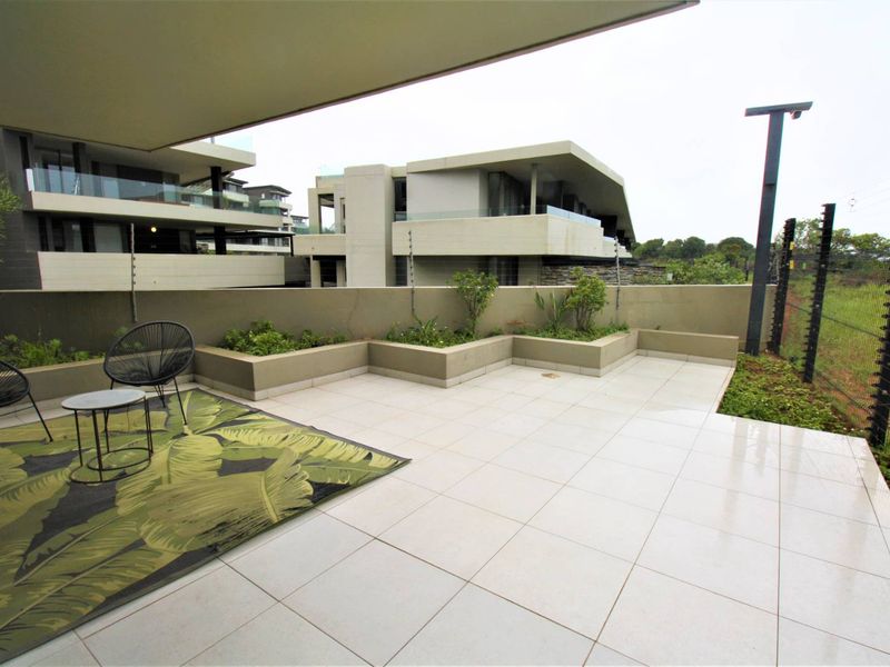A spacious, modern covered patio featuring tiled flooring and built-in planters, offering a clean outdoor living space with secure perimeter fencing.