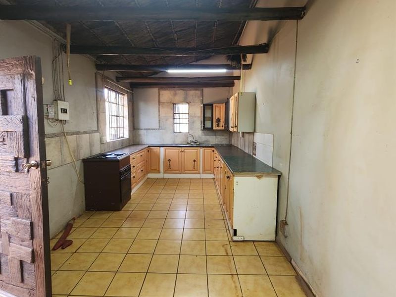 A spacious kitchen featuring tiled flooring, exposed timber ceiling beams, and built-in cabinetry, offering a functional layout ready for modernization and renovation.