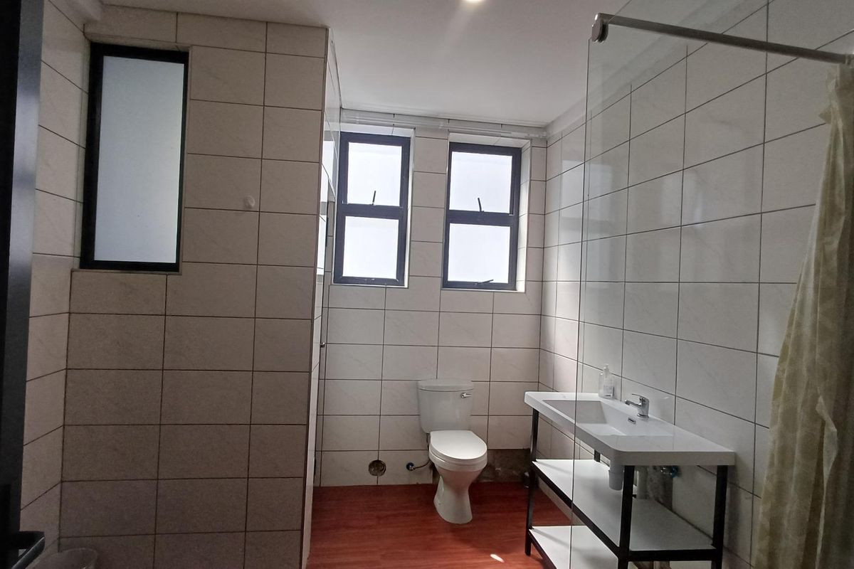 A functional bathroom featuring floor-to-ceiling wall tiles, a modern vanity with integrated basin, a glass shower screen, and a toilet.