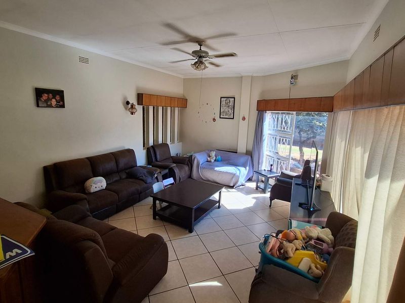 Spacious living room featuring tiled flooring, a ceiling fan, and large windows with built-in pelmets, offering a functional and comfortable family space.