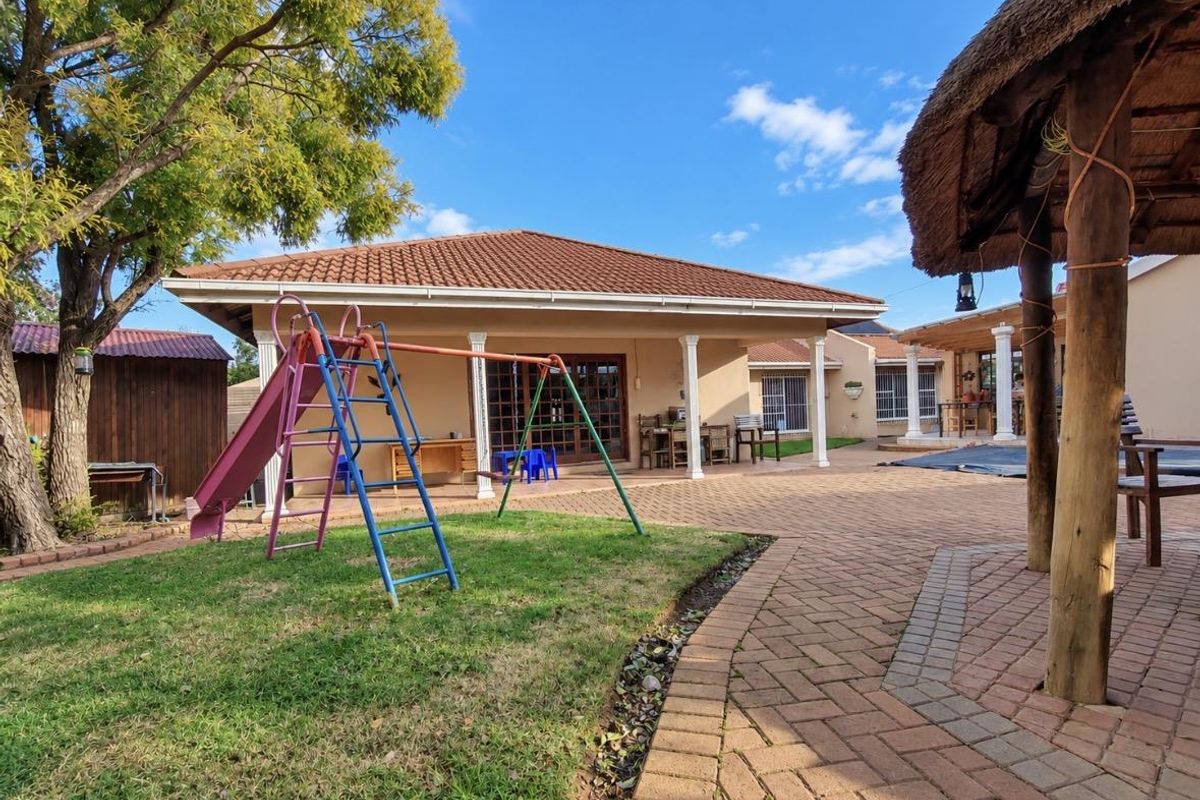 Spacious rear garden featuring a paved patio area, a covered veranda with columns, and a traditional thatched lapa structure.