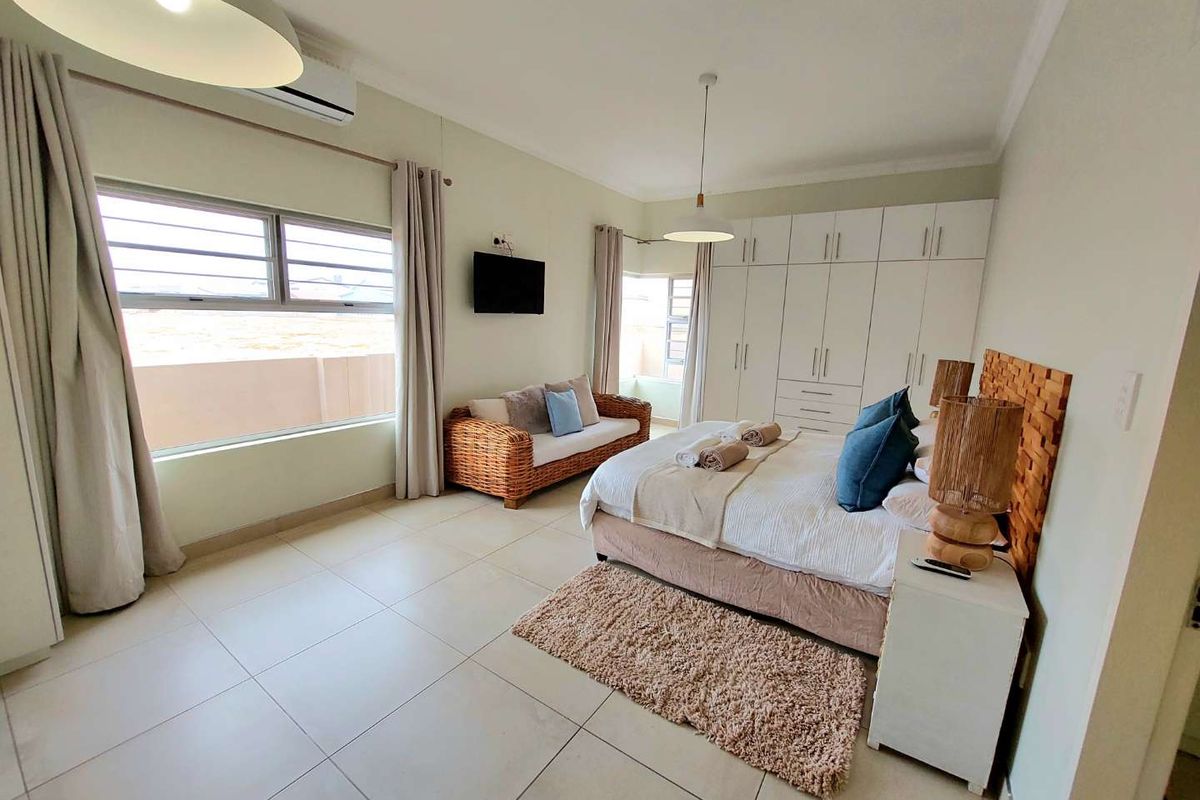 Spacious bedroom featuring large format floor tiles, built-in floor-to-ceiling wardrobes, and a wall-mounted air conditioning unit.