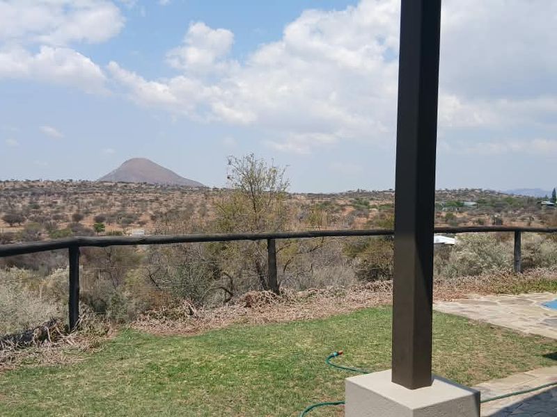A covered patio area featuring stone paving and timber railings, overlooking a scenic landscape with a swimming pool visible in the foreground.