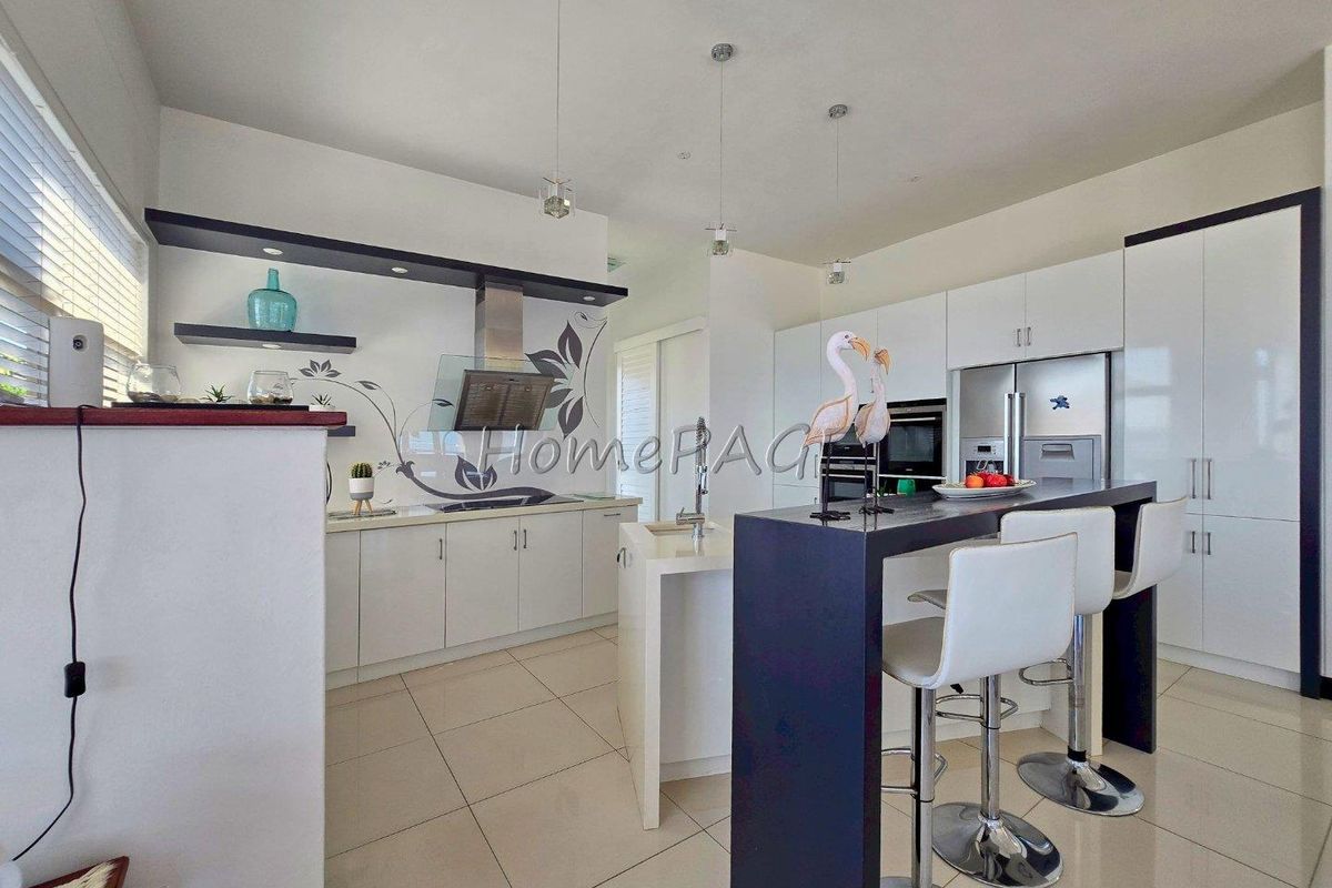 Modern kitchen featuring white cabinetry, a central island with breakfast bar, built-in oven, and stainless steel extractor fan with tiled flooring.