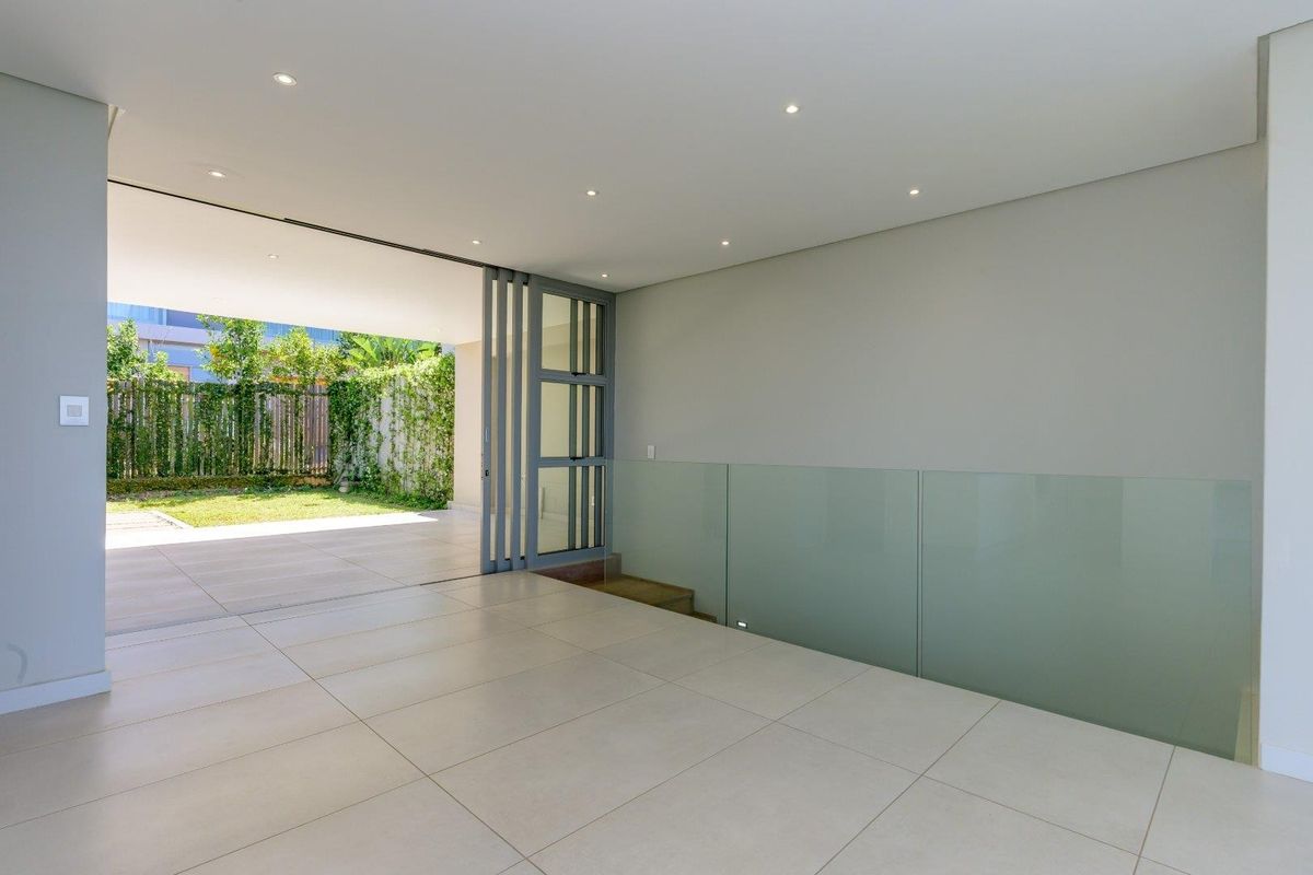 A bright, modern open-plan living area featuring large sliding glass doors that open onto a patio, with sleek tiled floors and a glass balustrade.