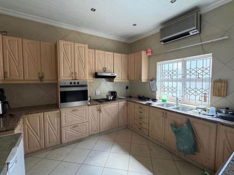 A functional kitchen featuring light wood cabinetry, granite countertops, built-in oven, extractor fan, and a double sink with security bars on the window.
