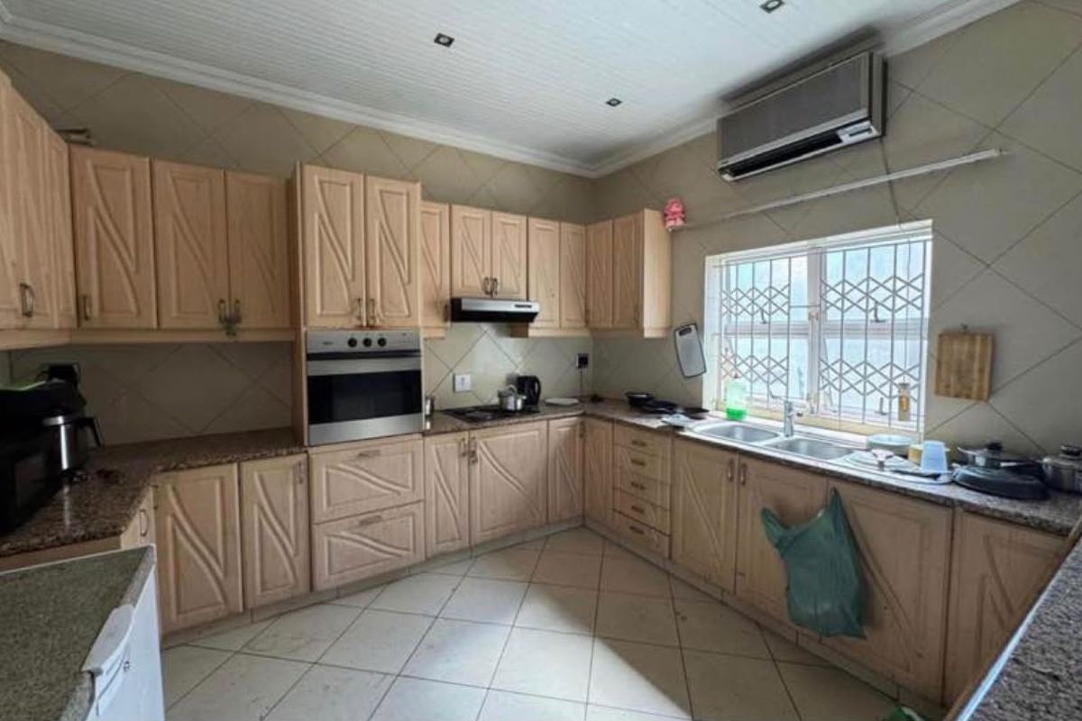 A functional kitchen featuring light wood cabinetry, granite countertops, built-in oven, extractor fan, and a double sink with security bars on the window.