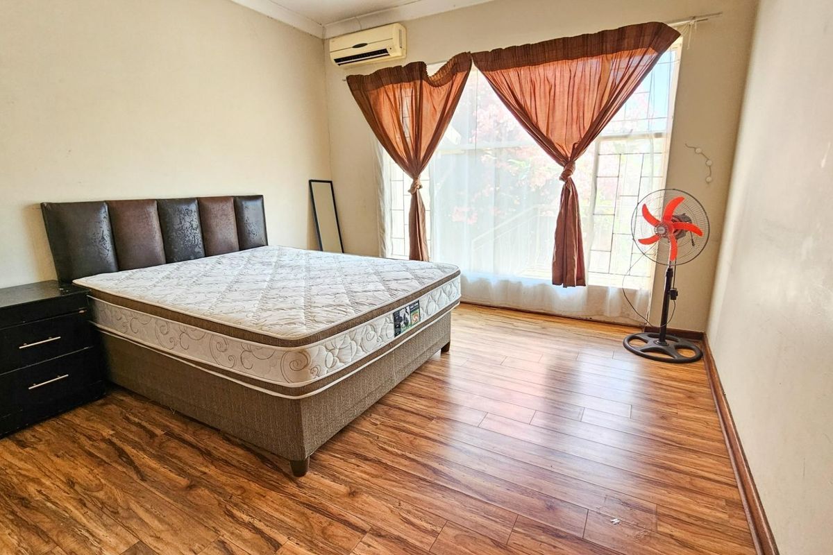 A bedroom featuring wood-look laminate flooring, a wall-mounted air conditioning unit, and a large window with security bars.