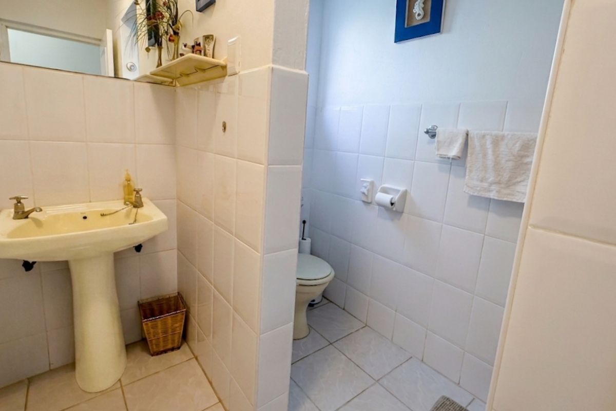A functional bathroom featuring a pedestal basin and a separate toilet area with white wall tiling and tiled flooring.