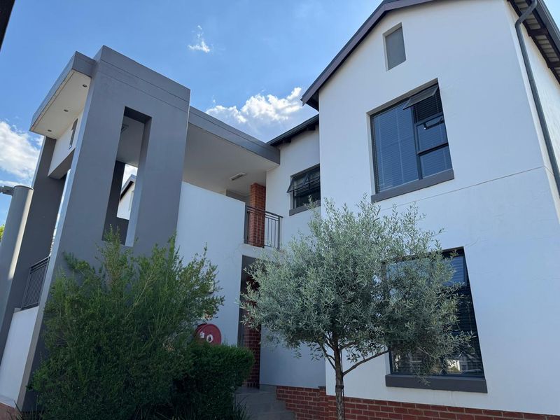 Modern apartment building exterior featuring a combination of white plaster, grey architectural accents, and brick detailing with aluminium window frames.