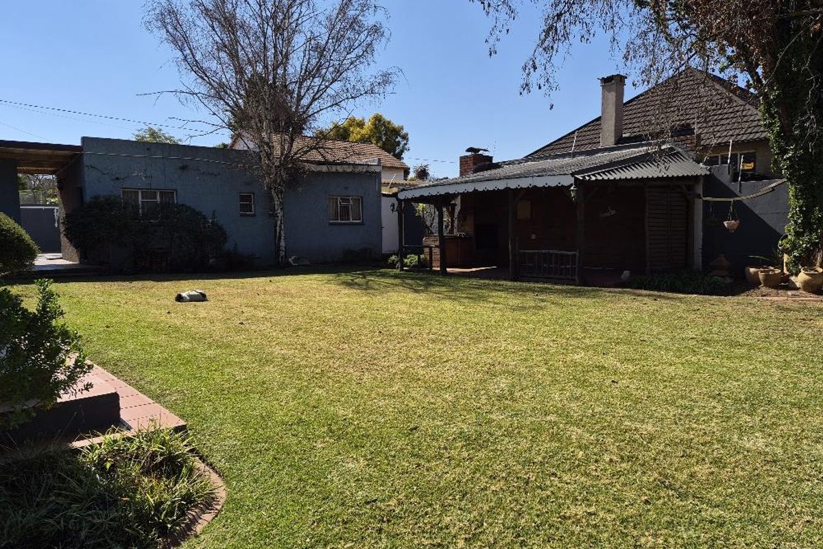 Spacious rear garden featuring a well-maintained lawn and a covered patio area with a built-in braai, ideal for outdoor entertaining.