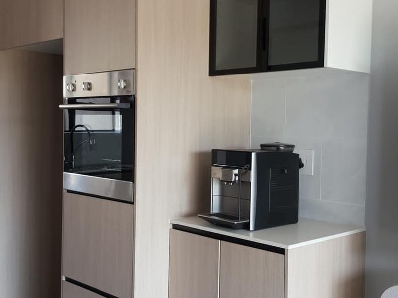 Modern kitchen featuring light wood-tone cabinetry, integrated oven, stone countertops, and sleek glass-fronted upper cabinets in a clean, contemporary design.