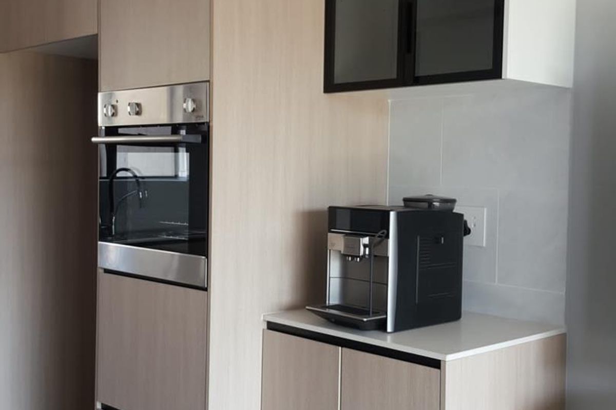 Modern kitchen featuring light wood-tone cabinetry, integrated oven, stone countertops, and sleek glass-fronted upper cabinets in a clean, contemporary design.