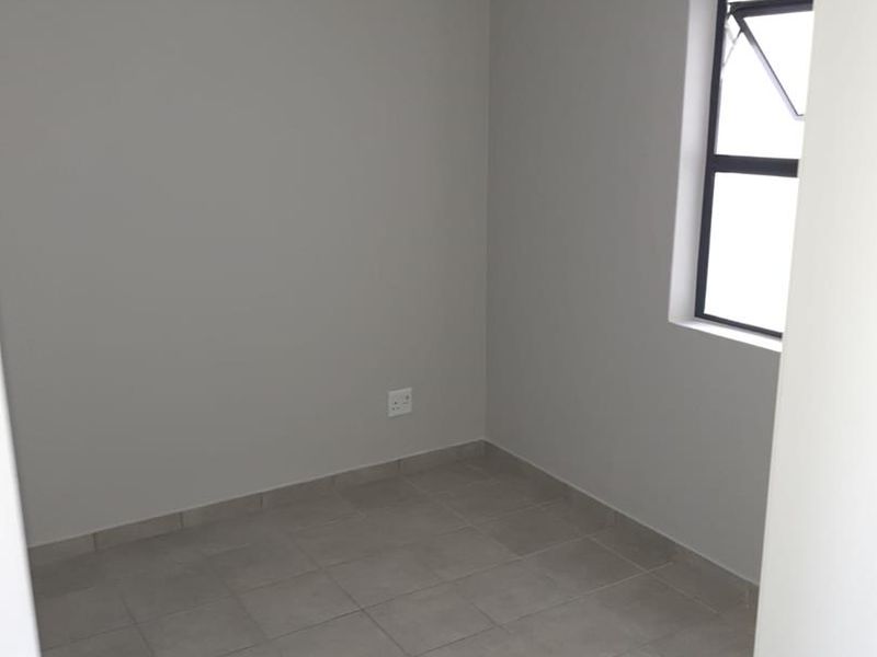 A clean, empty bedroom featuring neutral wall paint, tiled flooring, and a functional window with a curtain track installed.
