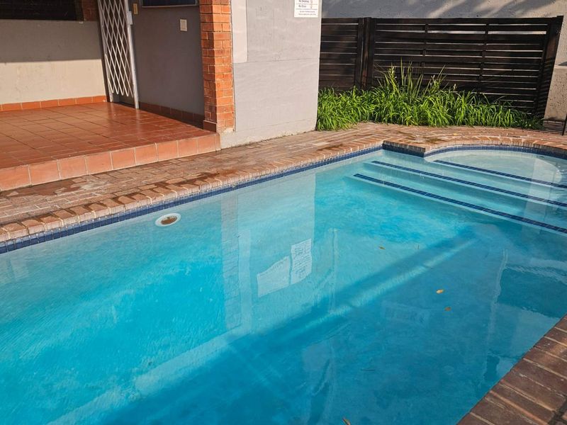 A private swimming pool area featuring brick coping, adjacent tiled patio space, and secure perimeter fencing.