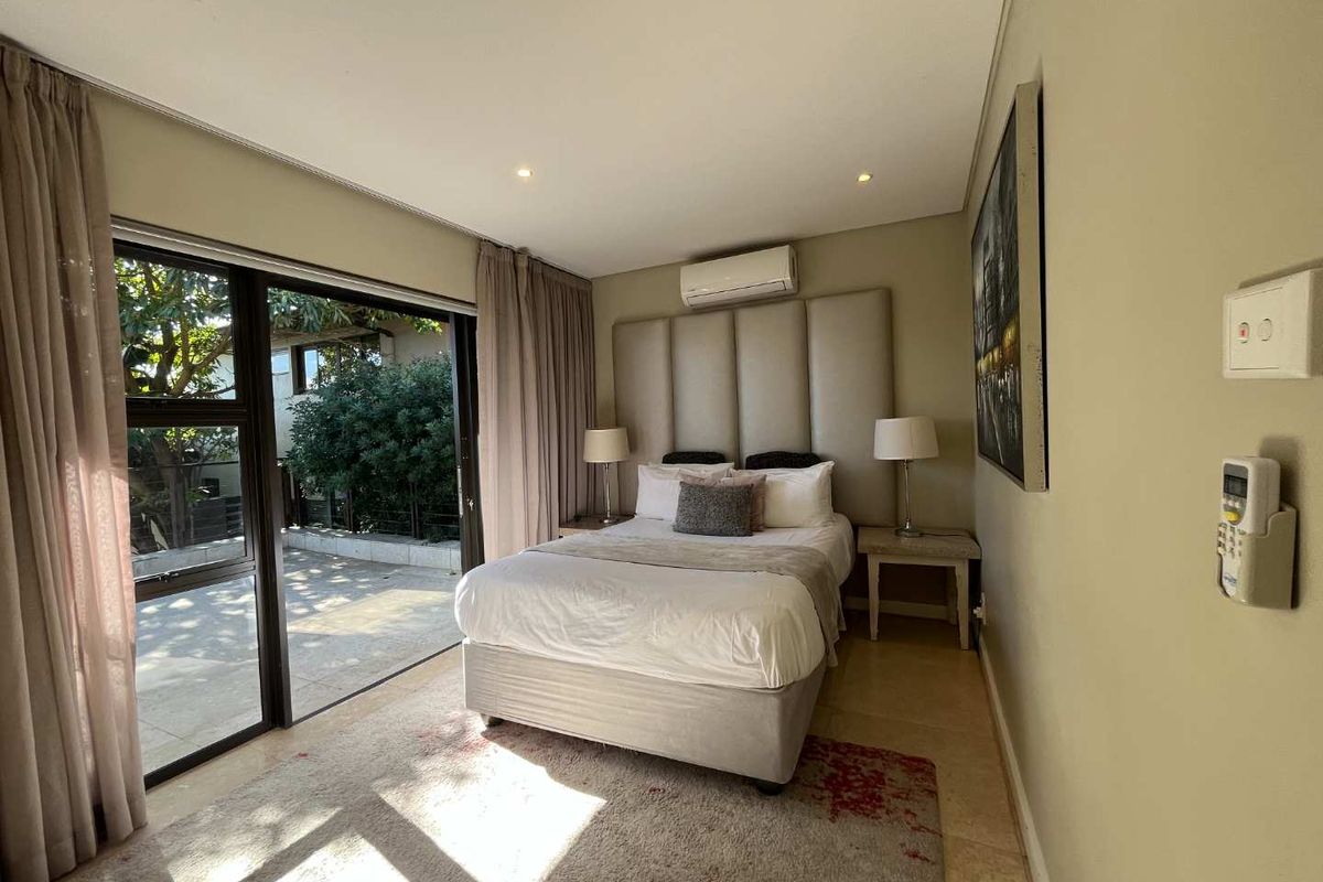 A well-maintained bedroom featuring a built-in headboard, recessed ceiling lighting, and large sliding glass doors providing direct access to an outdoor patio area.