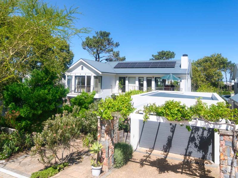 Elevated view of a well-maintained residential property featuring a metal roof with solar panels, a stone-pillared pergola, and a paved driveway.