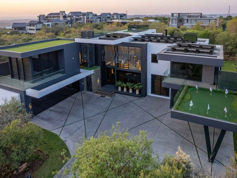 Aerial view of a modern luxury residence featuring a concrete driveway, integrated putting green, and contemporary architectural design with flat roof sections.