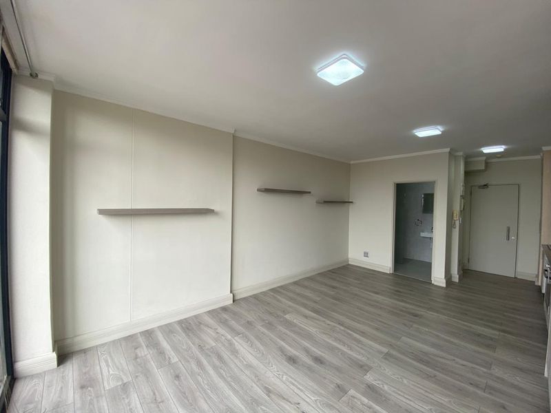 An open-plan living area featuring modern laminate flooring, neutral walls, and floating shelves, providing a clean and versatile space.