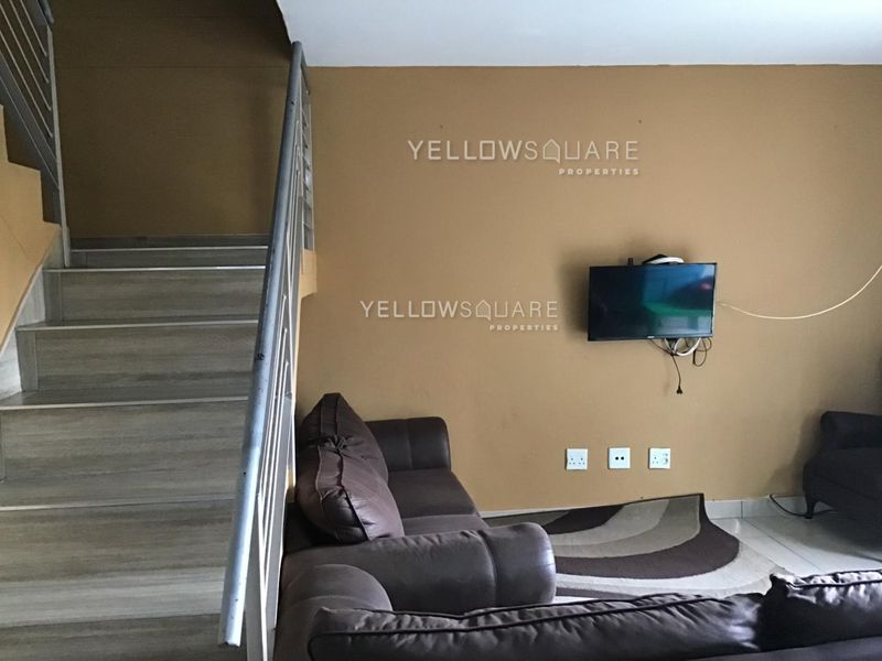 Living room area featuring a staircase with a metal handrail, tiled flooring, and wall-mounted electrical points.