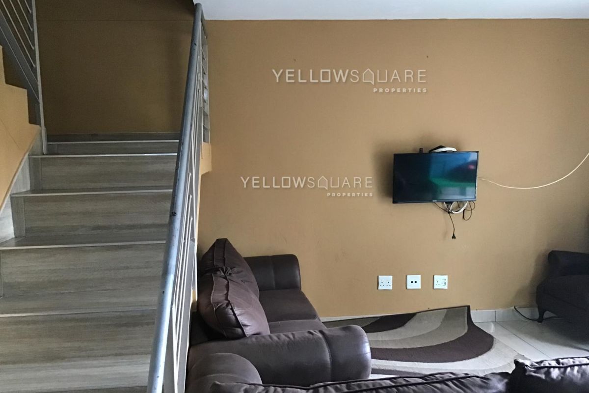 Living room area featuring a staircase with a metal handrail, tiled flooring, and wall-mounted electrical points.