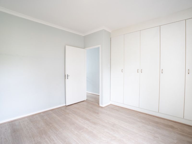 A bright, empty bedroom featuring light-toned laminate flooring and extensive built-in cupboard storage.