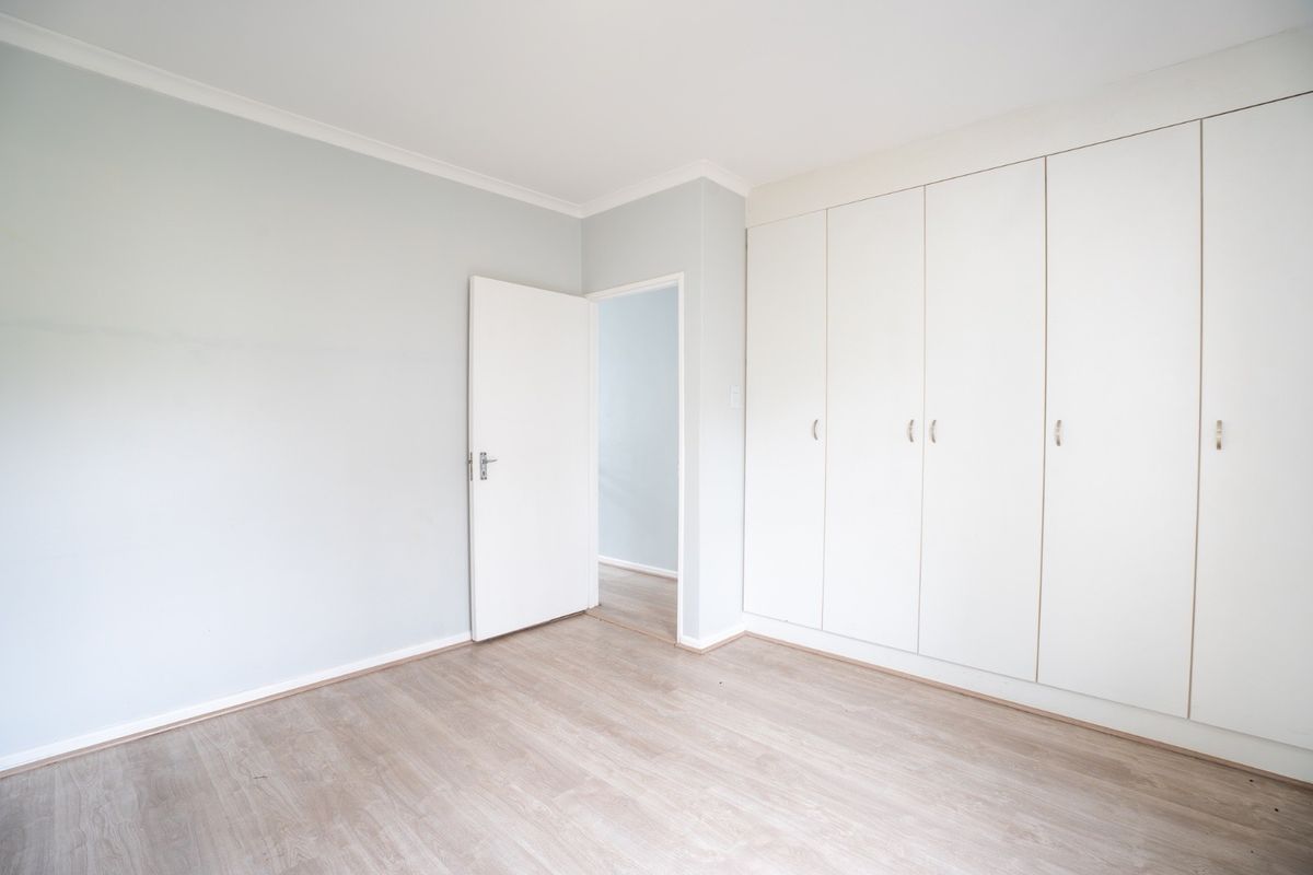 A bright, empty bedroom featuring light-toned laminate flooring and extensive built-in cupboard storage.