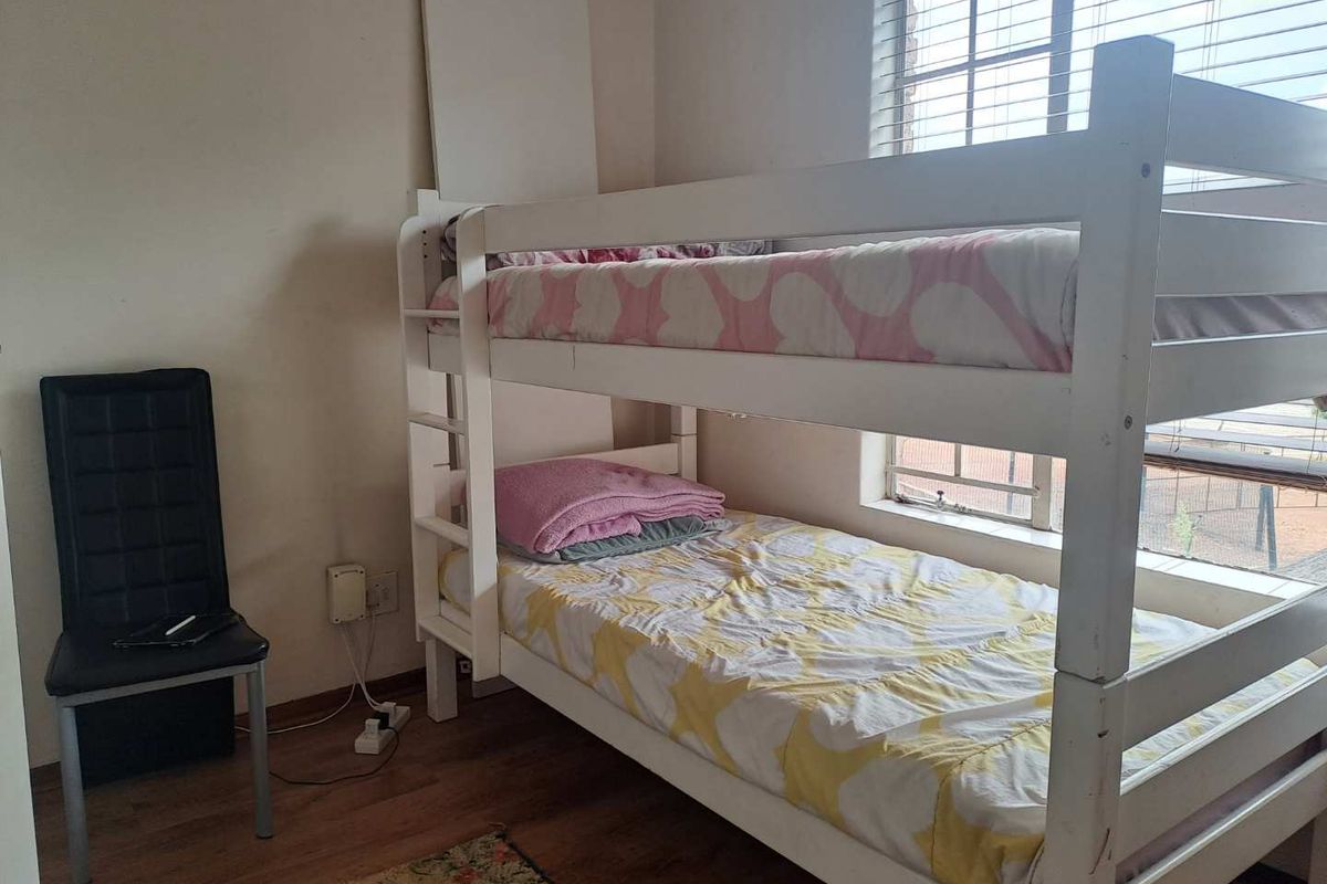 A functional bedroom featuring laminate flooring and a window with fitted blinds, providing natural light.
