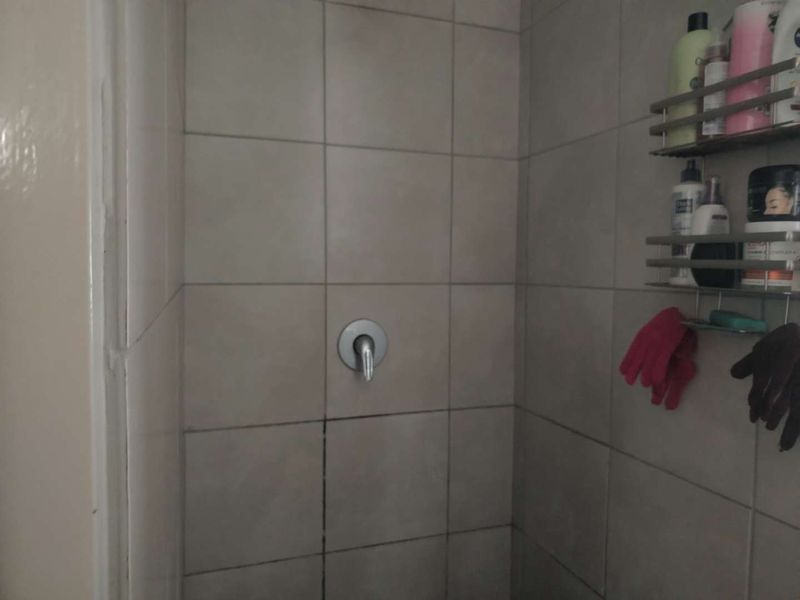 A close-up view of a shower enclosure featuring ceramic wall tiles and a single-lever shower mixer.