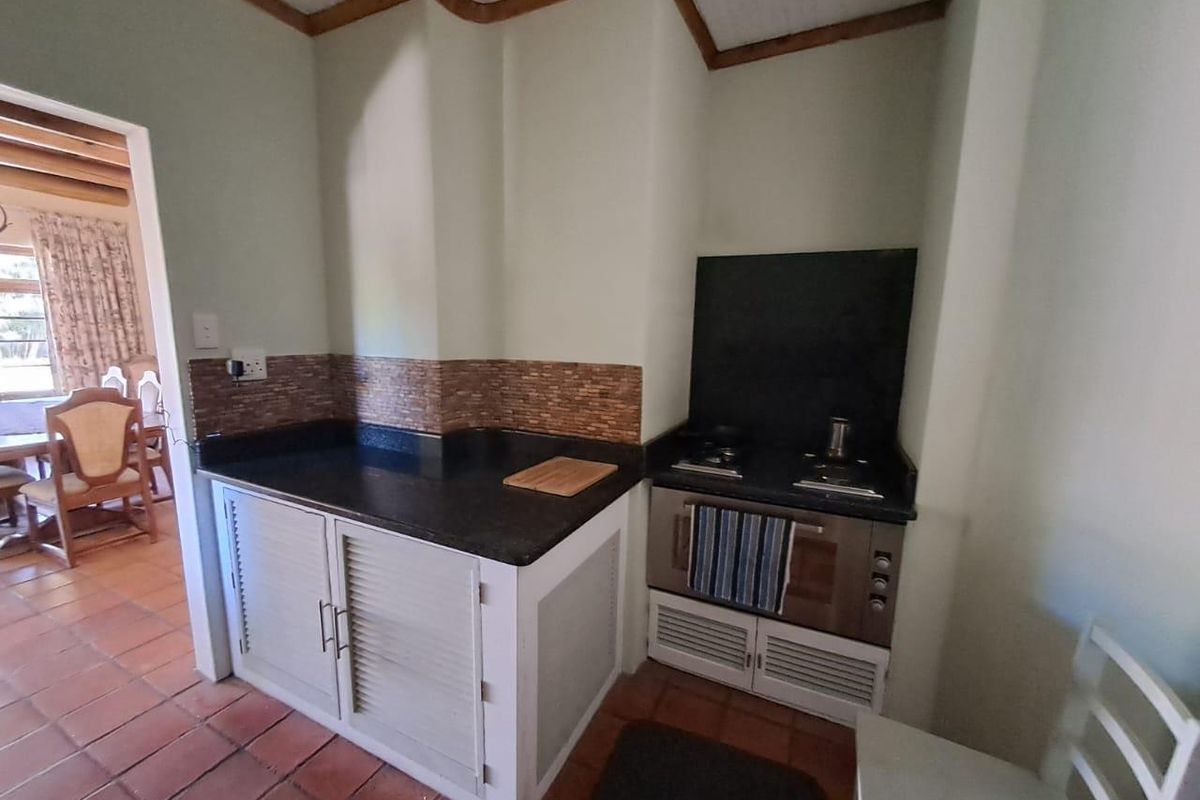 A compact kitchen area featuring built-in cabinetry, a dark stone countertop, and a built-in oven with a hob, finished with terracotta floor tiles.
