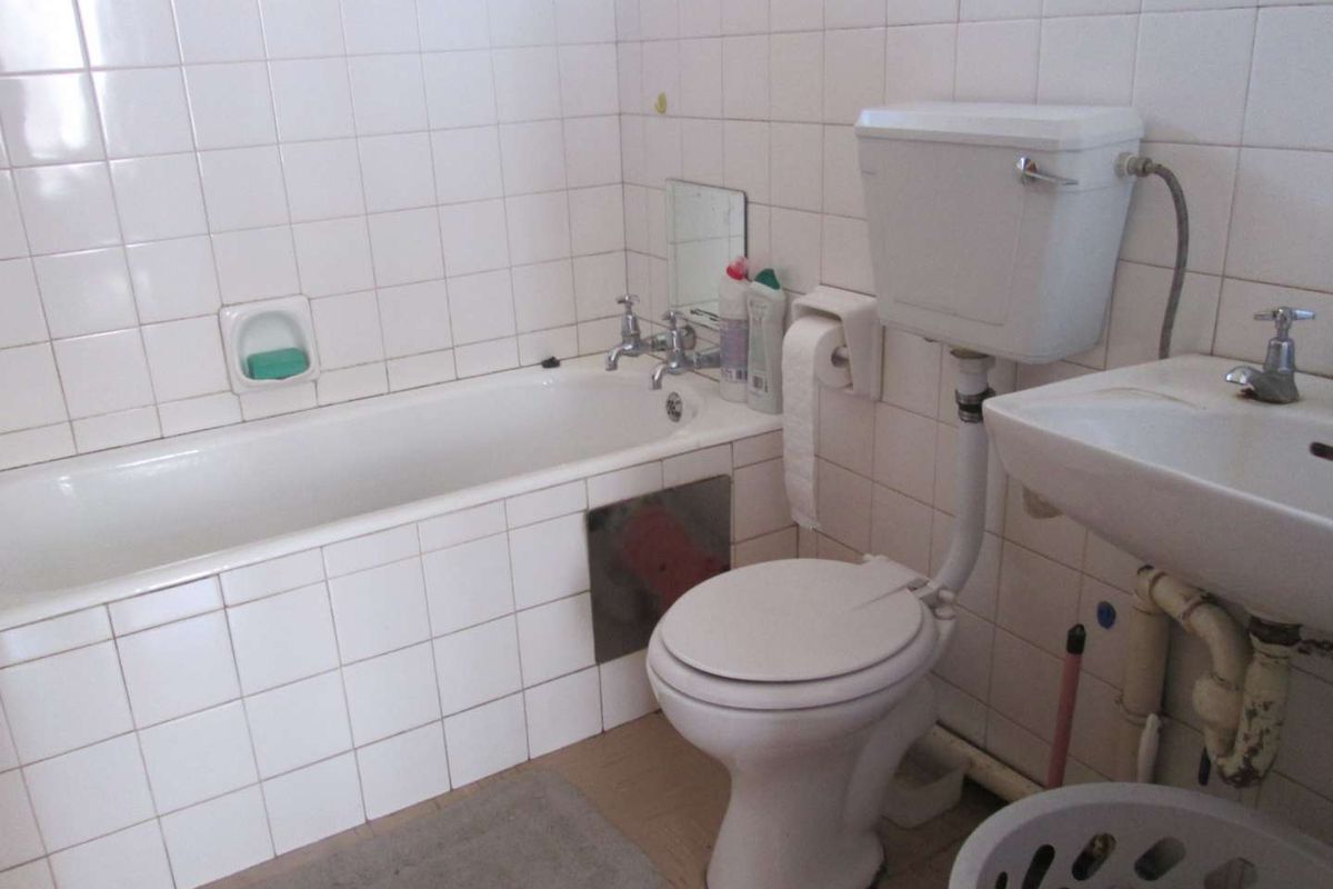 A dated bathroom featuring a standard bathtub, pedestal basin, and toilet with white wall tiling throughout.