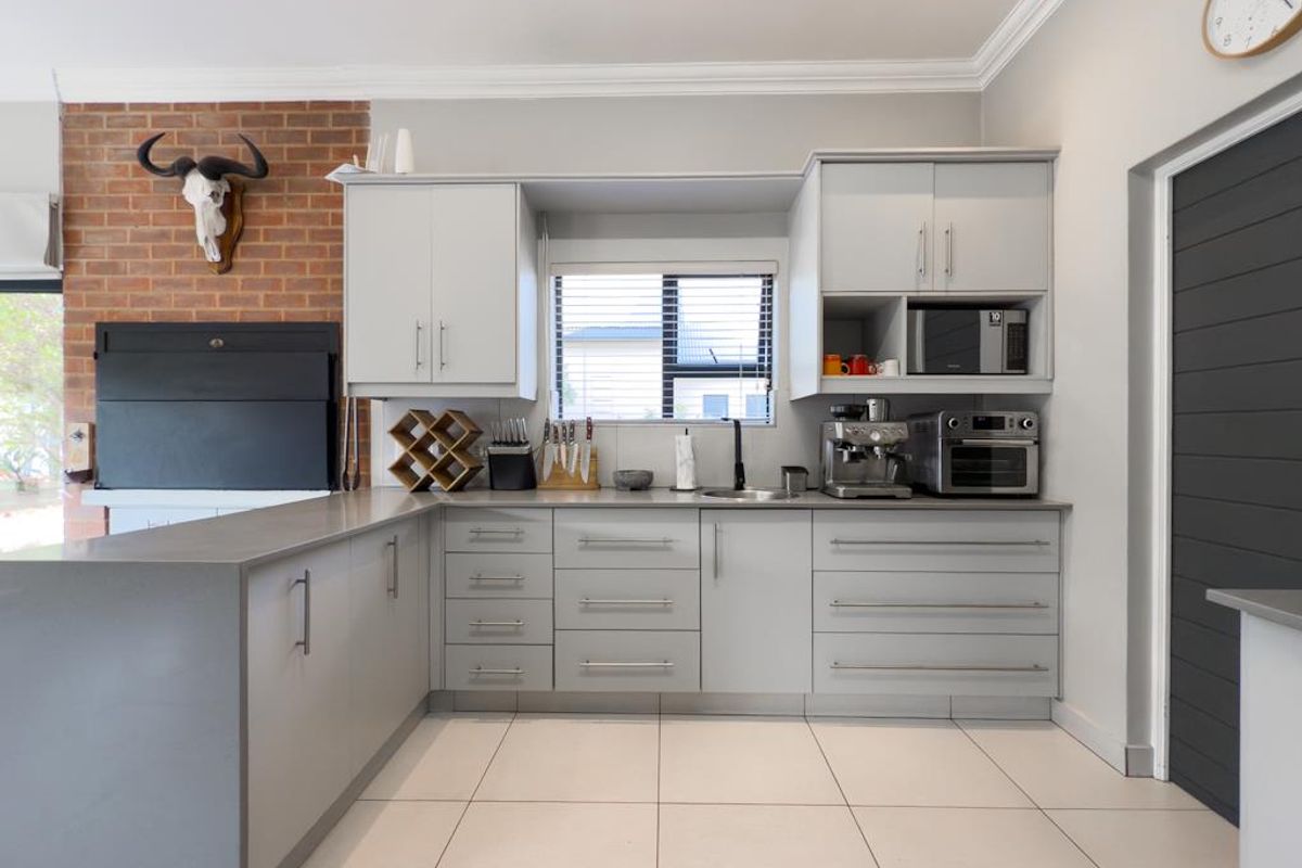 Modern kitchen featuring light grey cabinetry, stone countertops, integrated sink, and a built-in indoor braai fireplace with a brick feature wall.