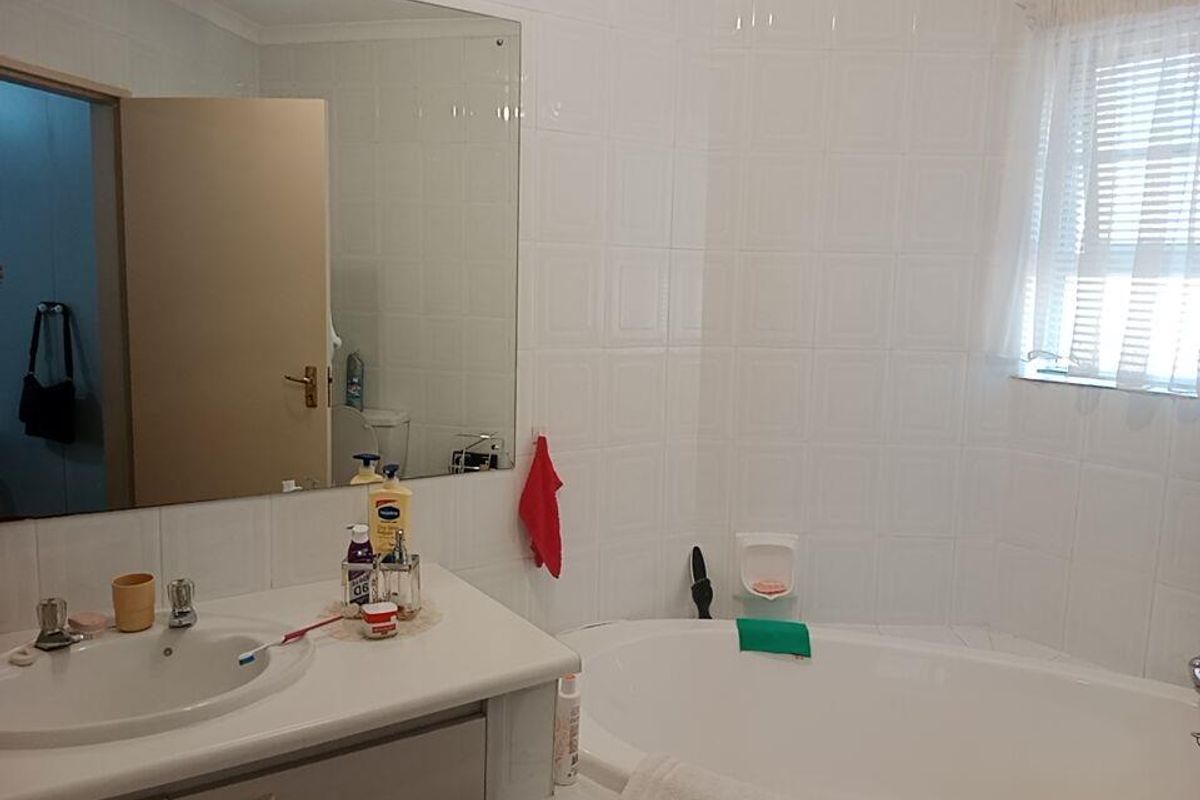 A functional bathroom featuring a built-in vanity with a basin, a large wall-mounted mirror, and a bathtub with tiled surround.