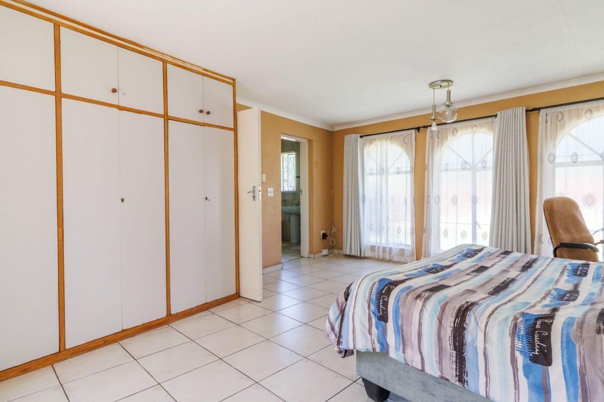 Spacious bedroom featuring built-in floor-to-ceiling wardrobes, tiled flooring, and large arched windows allowing for natural light.