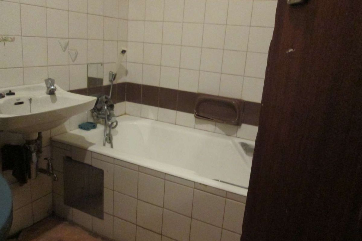 A dated bathroom featuring a bathtub and wall-mounted basin with tiled walls, requiring renovation to update the finishes and fixtures.