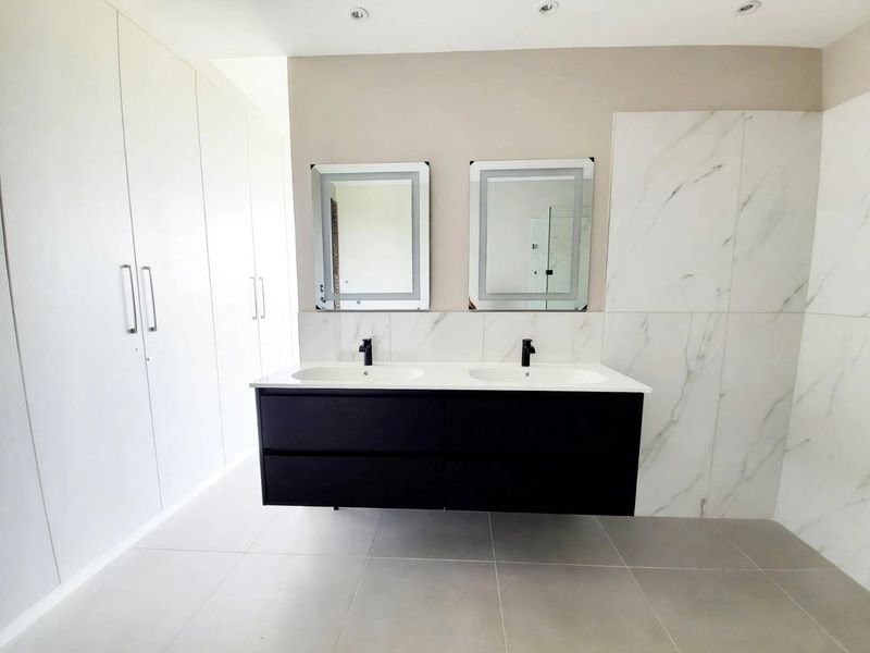 Modern bathroom featuring a sleek double vanity with black cabinetry, marble-look wall tiling, and extensive built-in storage cupboards.