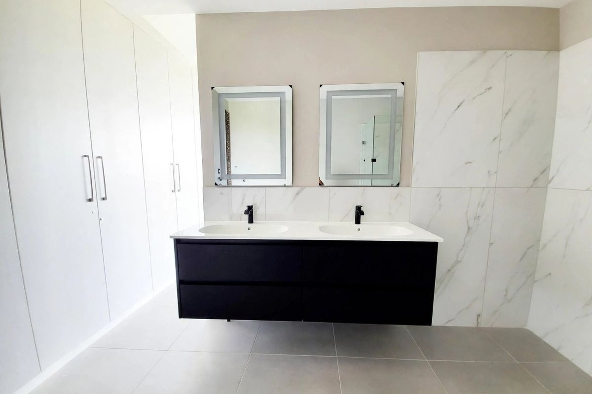 Modern bathroom featuring a sleek double vanity with black cabinetry, marble-look wall tiling, and extensive built-in storage cupboards.