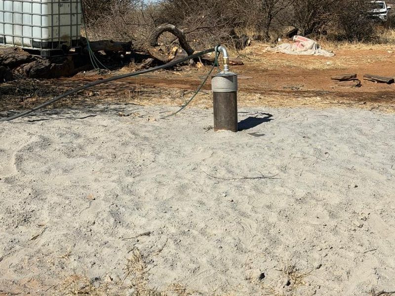 Agricultural land featuring a functional borehole with a connected water storage tank, situated in a natural, undeveloped landscape.
