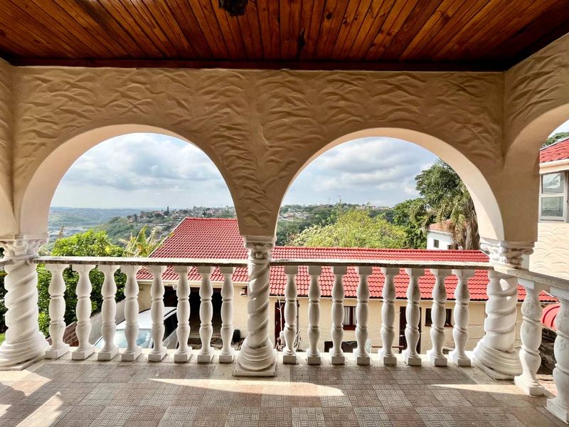 A covered balcony featuring decorative arched columns, a classic balustrade railing, and a timber ceiling, offering elevated views of the surrounding neighborhood.