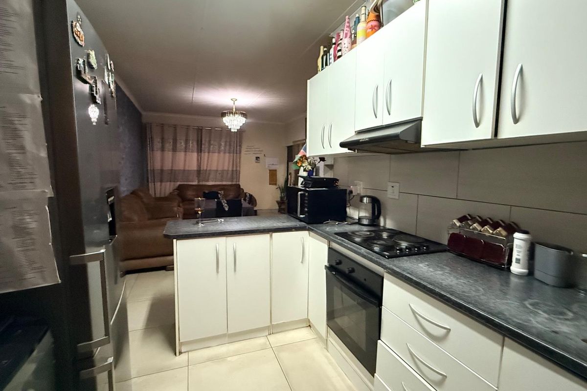Open-plan kitchen and living area featuring white cabinetry, dark laminate countertops, built-in oven, electric hob, and tiled flooring throughout.