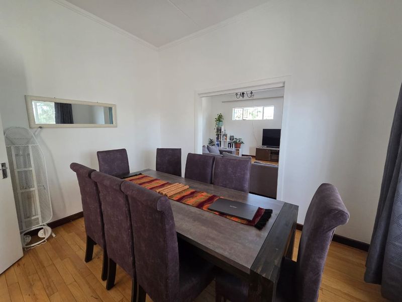 A dining room featuring hardwood flooring and coved cornicing, with an open transition into the adjacent living area.