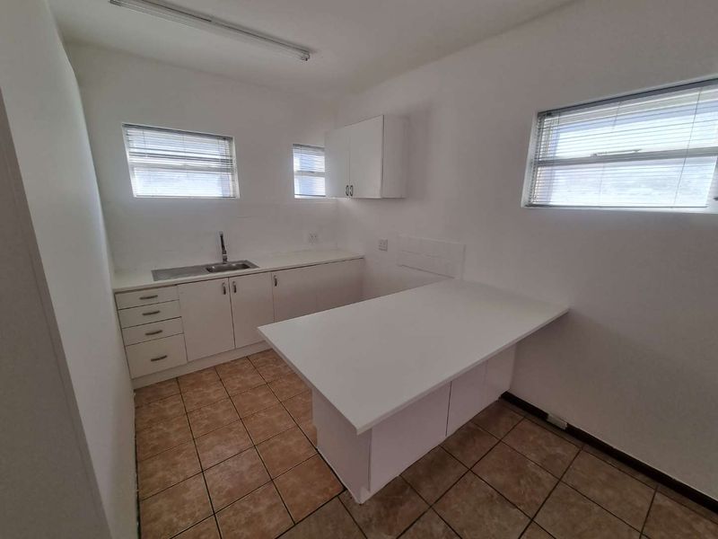 A functional, empty kitchen featuring white built-in cabinetry, a stainless steel sink, a breakfast bar, and tiled flooring.