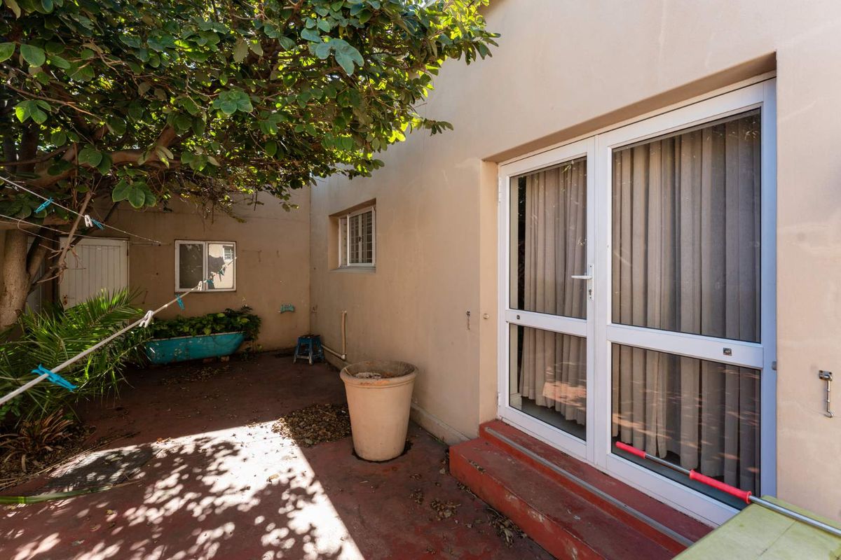 A private rear courtyard area featuring paved flooring, established tree cover, and direct access to the interior via double glass doors.