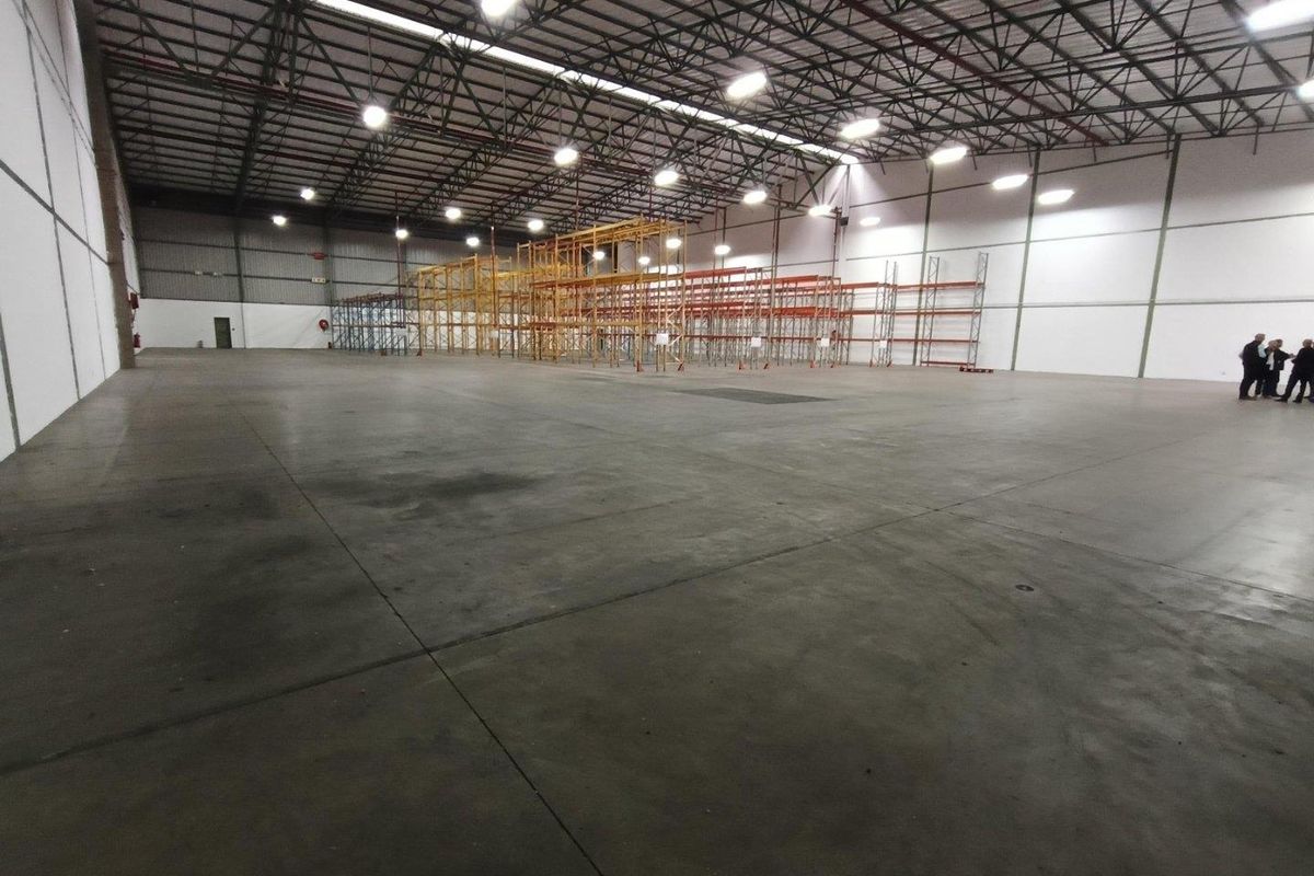 Spacious industrial warehouse featuring high ceilings, exposed steel trusses, high-bay lighting, and extensive built-in steel racking systems on a durable concrete floor.