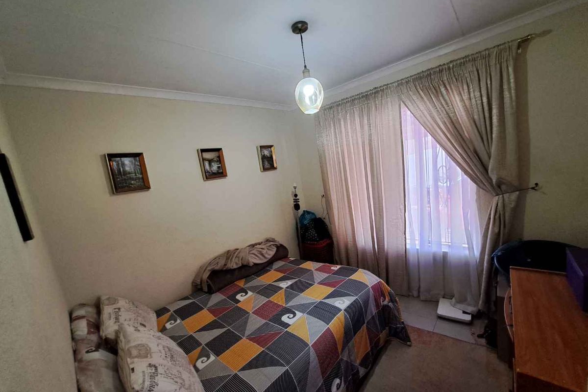 A standard bedroom featuring neutral walls, a central pendant light fixture, and window treatments with curtain rails.