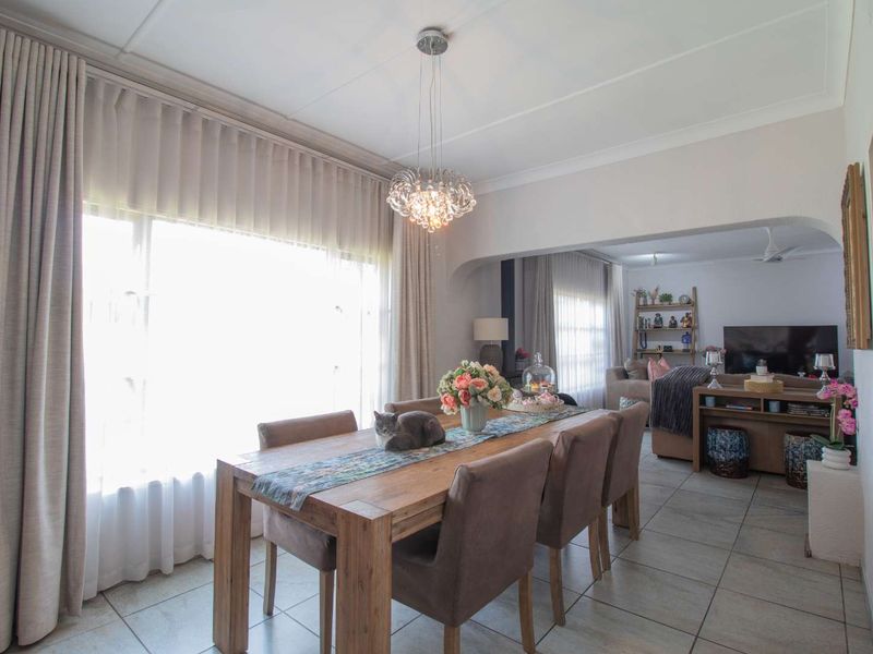 An open-plan dining and living area featuring tiled flooring, a decorative pendant light, and a spacious archway connecting the two living spaces.
