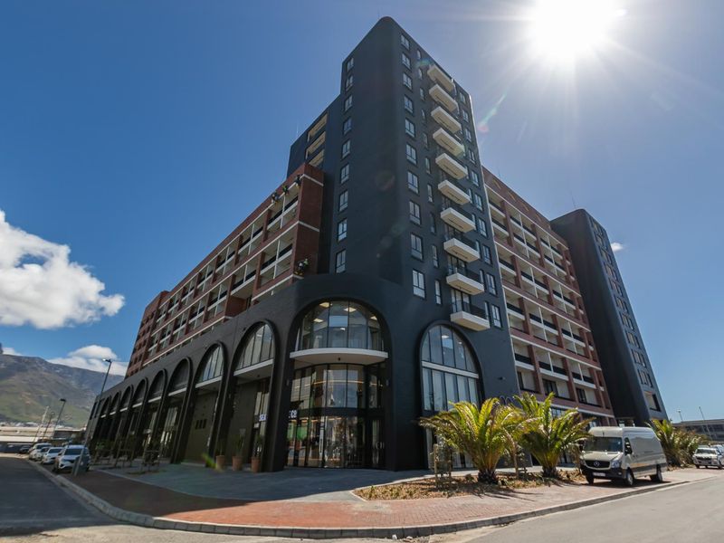 A modern multi-story apartment building featuring a striking dark facade, arched ground-level windows, and private balconies, situated on a corner lot.