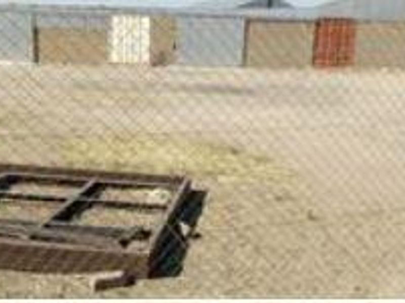 View of an industrial yard featuring metal cladding, multiple roller doors, and a chain link fence perimeter.