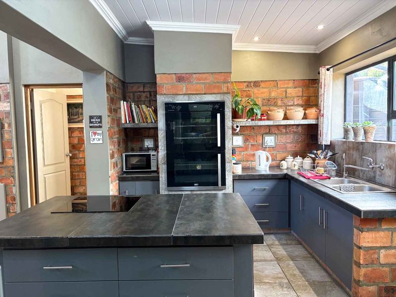 A rustic-style kitchen featuring exposed brick walls, dark cabinetry, a central island with a built-in hob, and a double wall oven.