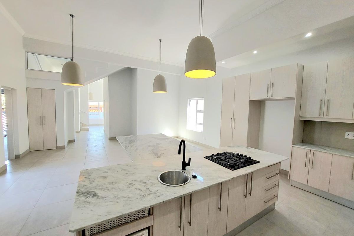 Modern open-plan kitchen featuring a central island with a built-in gas hob, sink, and stone countertops, complemented by light wood cabinetry.